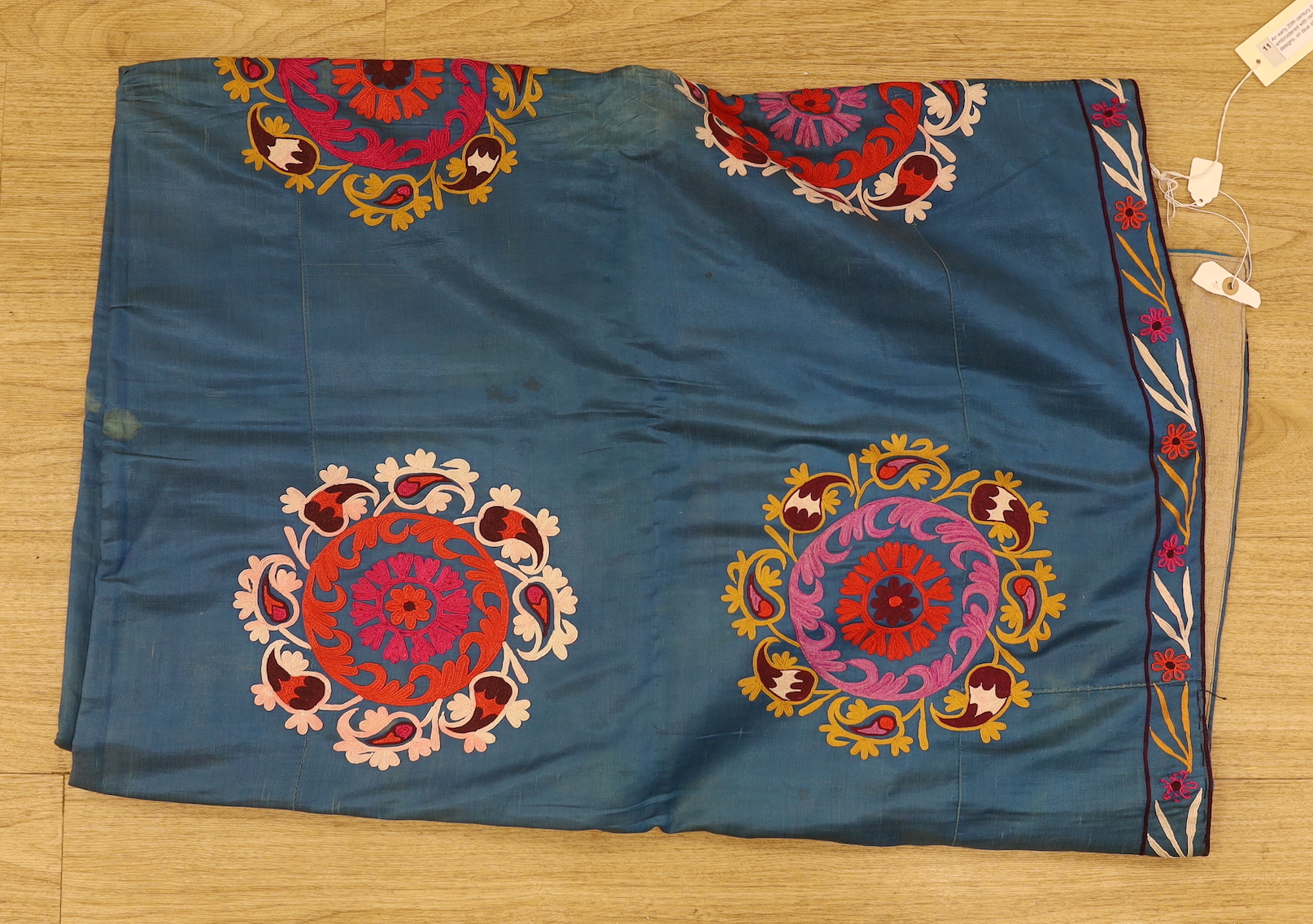 An early 20th century Suzani hanging, embroidered with red pink and gold foliate designs, on blue silk ground, 210 x 160cm